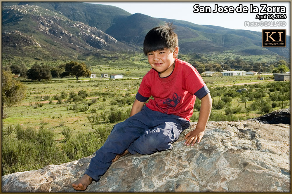 YOUNG INDIAN BOY POSING ON ROCK, Tribal ejido in background.